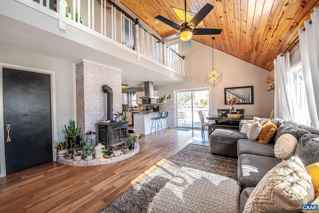 living room with wood-type flooring, ceiling fan, a wood stove, wood ceiling, and high vaulted ceiling