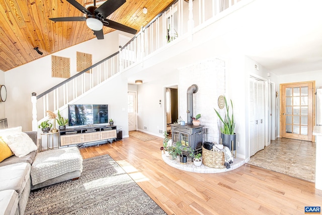 living room featuring a towering ceiling, wood ceiling, wood-type flooring, a wood stove, and ceiling fan