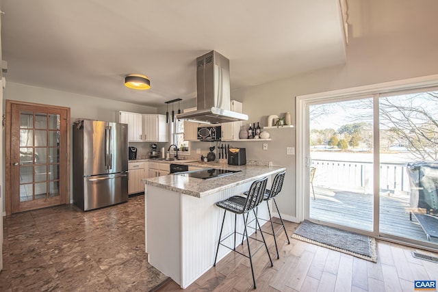 kitchen featuring kitchen peninsula, white cabinetry, island exhaust hood, black appliances, and a breakfast bar area