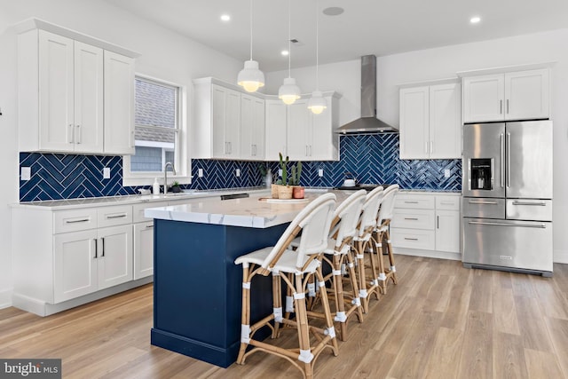 kitchen with wall chimney exhaust hood, a breakfast bar, high end refrigerator, a kitchen island, and pendant lighting