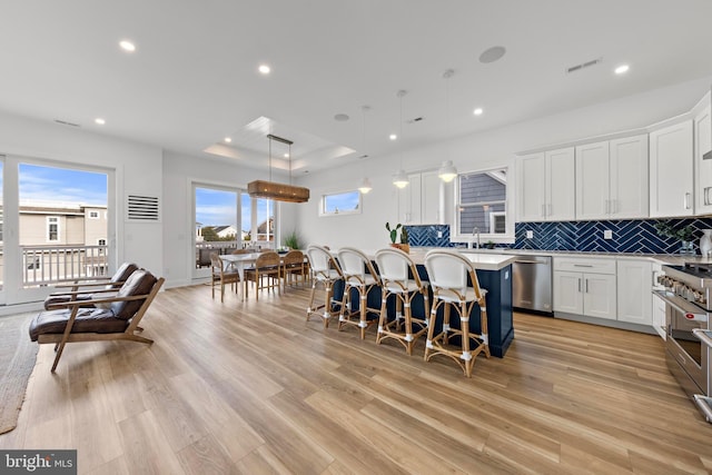 kitchen with white cabinetry, hanging light fixtures, appliances with stainless steel finishes, a kitchen island, and light hardwood / wood-style floors