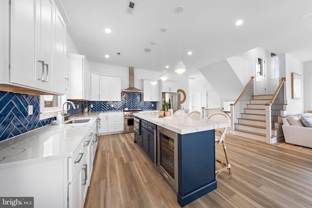 kitchen featuring pendant lighting, white cabinetry, sink, a center island with sink, and wall chimney range hood