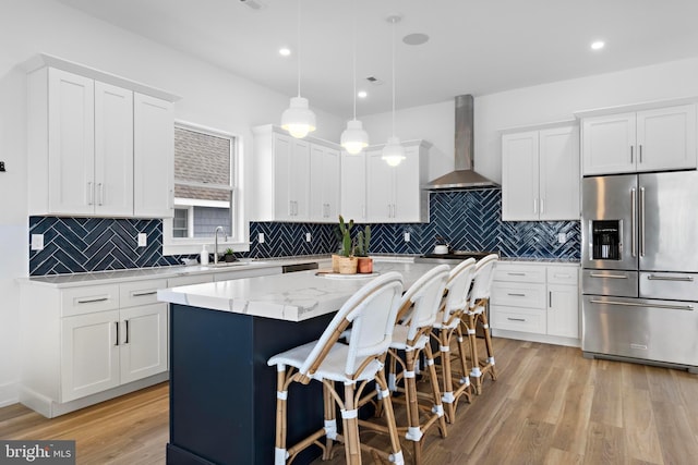 kitchen featuring pendant lighting, white cabinets, a center island, stainless steel fridge with ice dispenser, and wall chimney range hood