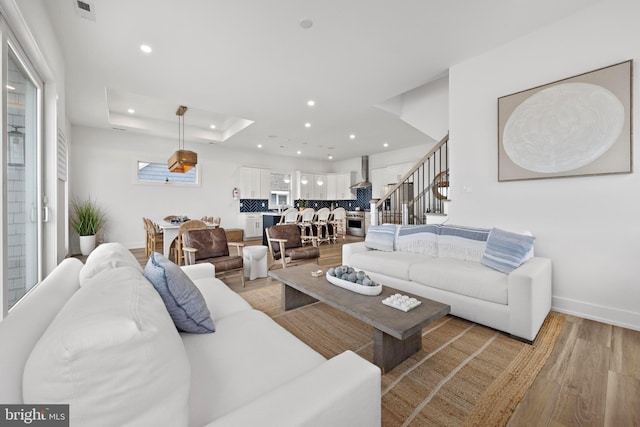 living room featuring a tray ceiling, light hardwood / wood-style flooring, and a healthy amount of sunlight