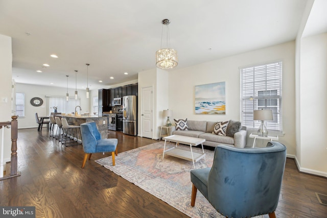 living room with sink, a notable chandelier, and dark wood-type flooring