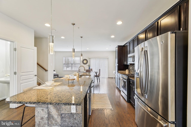 kitchen with pendant lighting, sink, a center island with sink, stainless steel appliances, and stone countertops