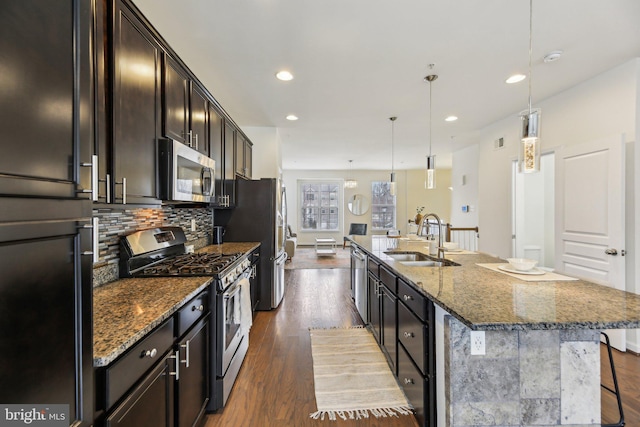 kitchen featuring appliances with stainless steel finishes, a breakfast bar, decorative light fixtures, sink, and a center island with sink