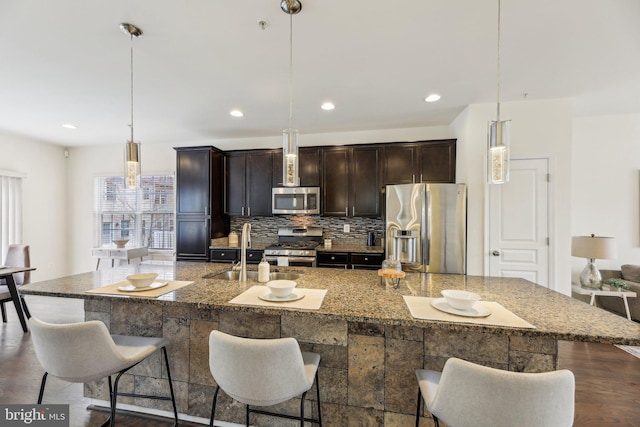 kitchen with hanging light fixtures, appliances with stainless steel finishes, and a kitchen island with sink