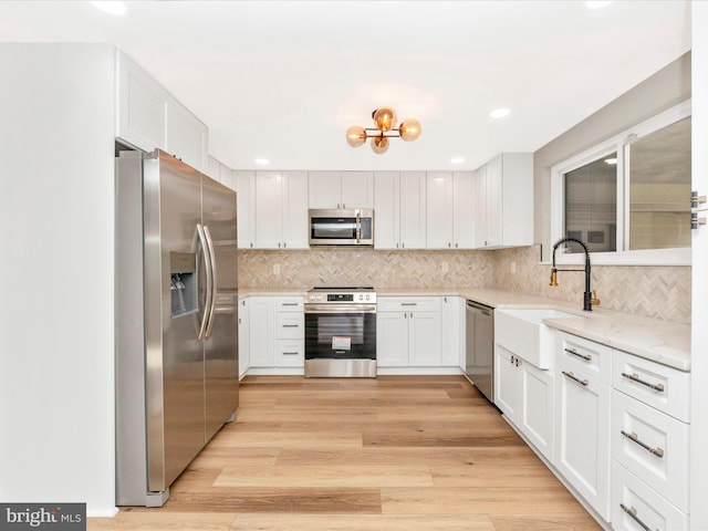 kitchen with white cabinetry, stainless steel appliances, sink, light wood-type flooring, and light stone counters