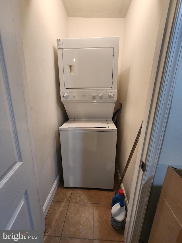 washroom with dark tile patterned flooring and stacked washer / dryer