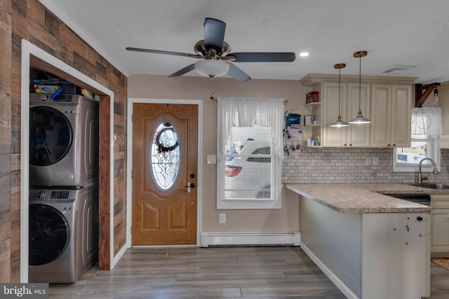 kitchen featuring a baseboard heating unit, cream cabinetry, stacked washing maching and dryer, and decorative light fixtures