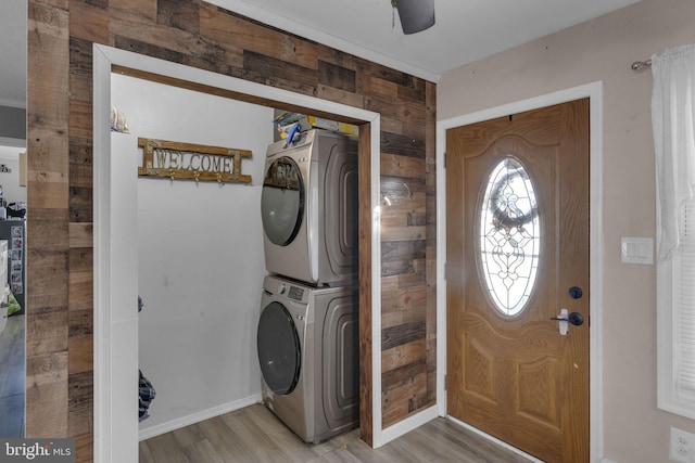 clothes washing area featuring stacked washer and dryer, light hardwood / wood-style flooring, and wooden walls