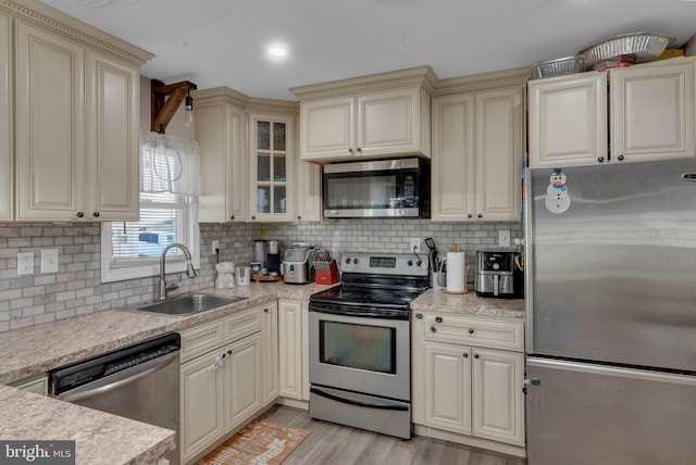 kitchen featuring light hardwood / wood-style floors, decorative backsplash, sink, appliances with stainless steel finishes, and cream cabinetry