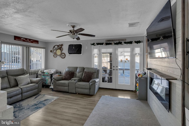 living room featuring a textured ceiling, ceiling fan, light hardwood / wood-style flooring, and french doors