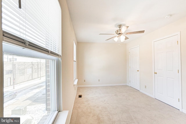 unfurnished bedroom featuring light carpet, ceiling fan, and multiple windows