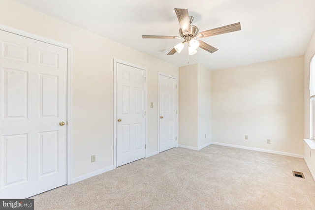 unfurnished bedroom with ceiling fan, light carpet, and multiple closets