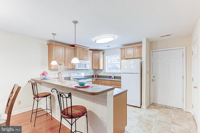 kitchen with white appliances, light brown cabinetry, a kitchen breakfast bar, hanging light fixtures, and kitchen peninsula