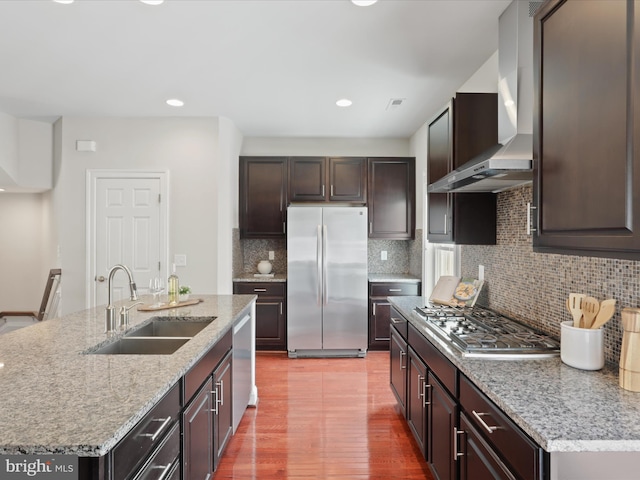 kitchen with appliances with stainless steel finishes, wall chimney range hood, tasteful backsplash, sink, and a kitchen island with sink