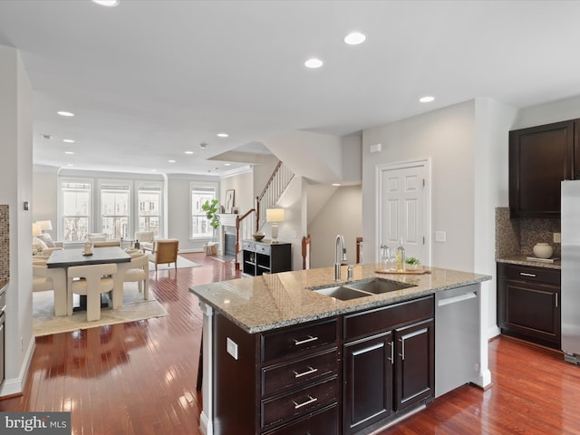 kitchen with appliances with stainless steel finishes, sink, backsplash, light stone countertops, and a center island with sink