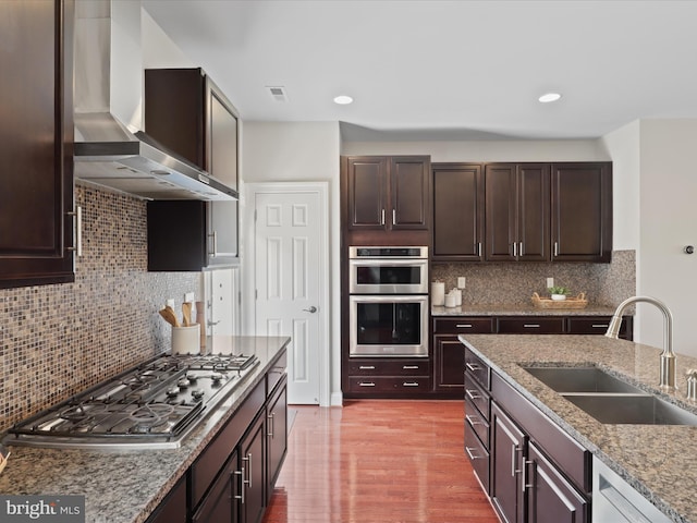 kitchen featuring light stone countertops, tasteful backsplash, sink, stainless steel appliances, and wall chimney exhaust hood