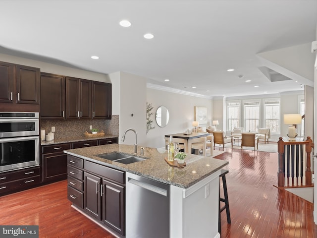 kitchen featuring appliances with stainless steel finishes, sink, backsplash, a kitchen island with sink, and a kitchen bar