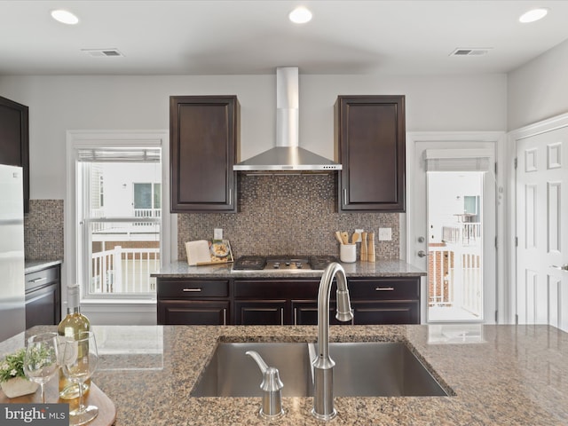 kitchen with tasteful backsplash, a healthy amount of sunlight, wall chimney range hood, stone counters, and stainless steel gas cooktop