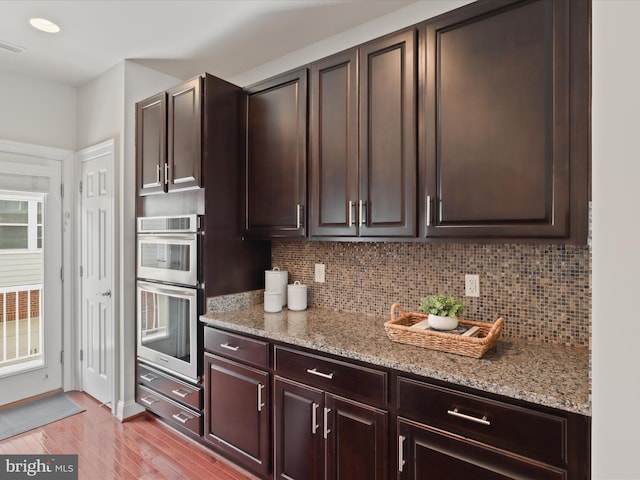 kitchen with light wood-type flooring, dark brown cabinets, stainless steel double oven, and light stone countertops