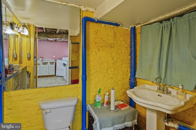 bathroom with brick wall, sink, independent washer and dryer, and toilet