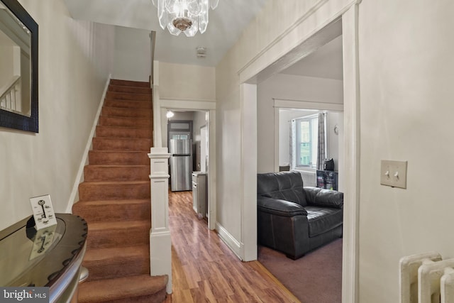 stairway featuring radiator heating unit, hardwood / wood-style floors, and a notable chandelier