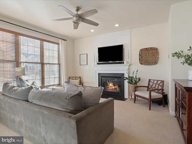 carpeted living room with ceiling fan and a large fireplace