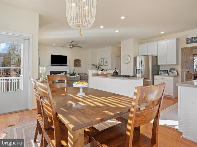 dining space with ceiling fan with notable chandelier and light hardwood / wood-style floors