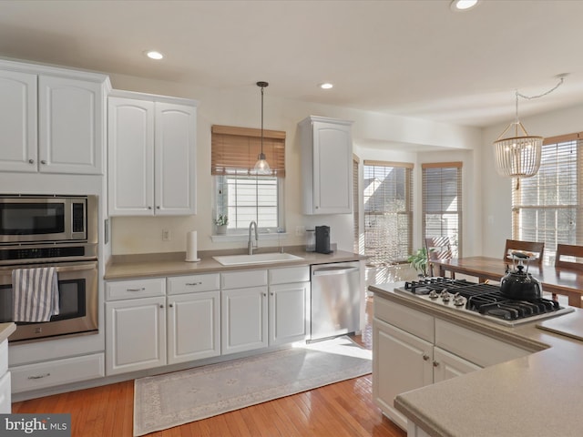 kitchen with appliances with stainless steel finishes, sink, white cabinets, and decorative light fixtures