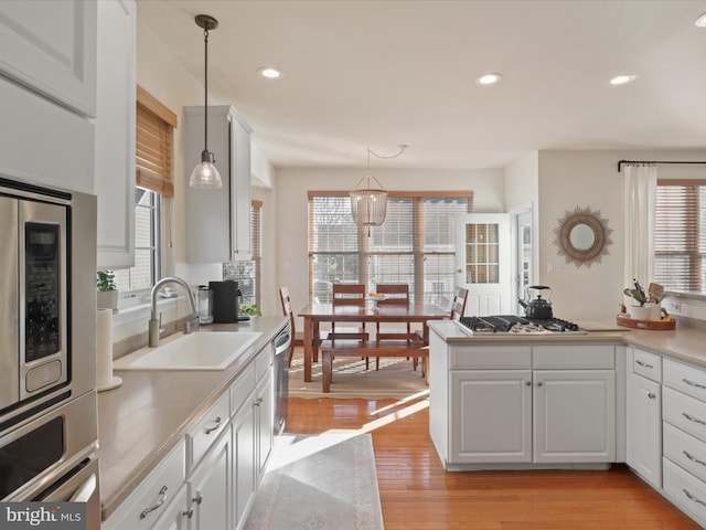 kitchen with pendant lighting, white cabinetry, sink, light hardwood / wood-style floors, and stainless steel appliances