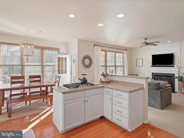 kitchen with stainless steel gas cooktop, white cabinetry, hanging light fixtures, light wood-type flooring, and kitchen peninsula