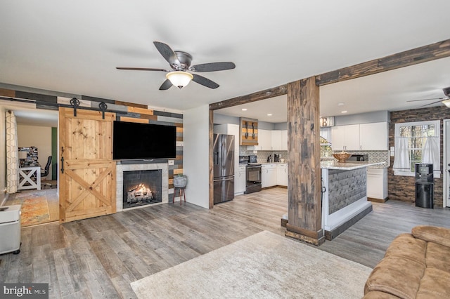 living room featuring light wood-type flooring, ceiling fan, beam ceiling, and a barn door