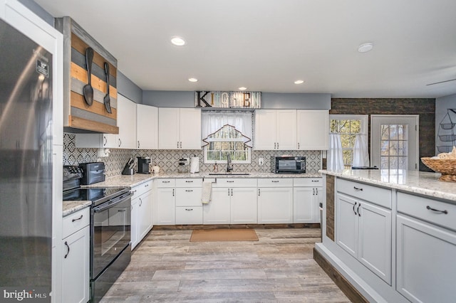 kitchen featuring fridge, sink, electric range, and white cabinetry