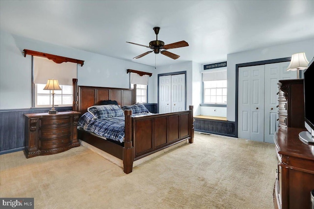 bedroom with ceiling fan, multiple windows, light carpet, and two closets