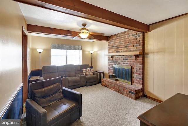 carpeted living room with wooden walls, ceiling fan, beam ceiling, and a brick fireplace