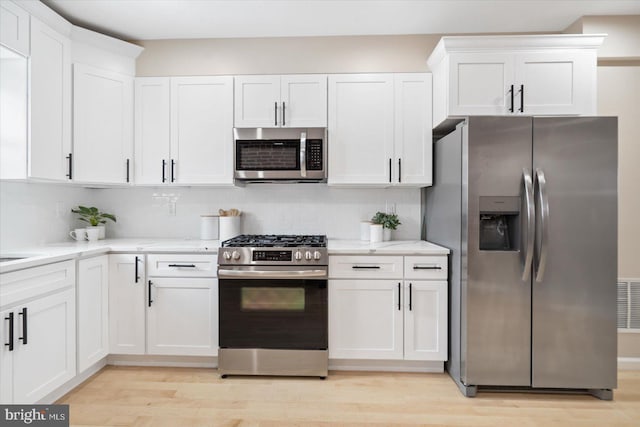 kitchen with light wood-type flooring, stainless steel appliances, decorative backsplash, and white cabinets