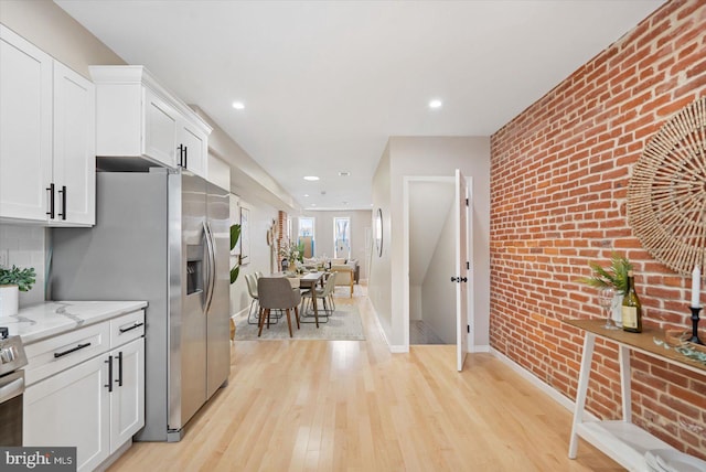 kitchen with white cabinets, light stone countertops, brick wall, and light hardwood / wood-style floors