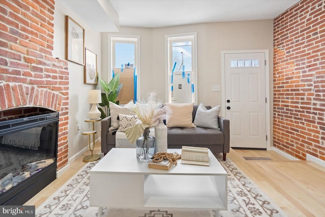 living room featuring a fireplace, brick wall, and light hardwood / wood-style floors