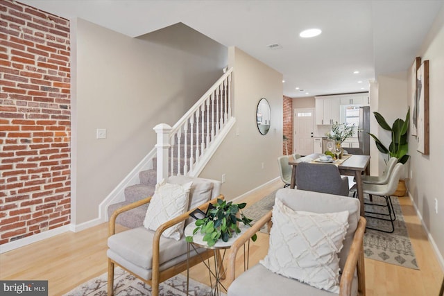 sitting room with brick wall and light hardwood / wood-style flooring