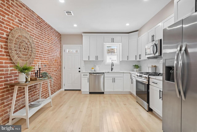 kitchen with backsplash, brick wall, stainless steel appliances, and white cabinetry