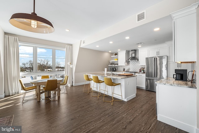 kitchen featuring high end refrigerator, white cabinetry, wall chimney exhaust hood, and light stone counters