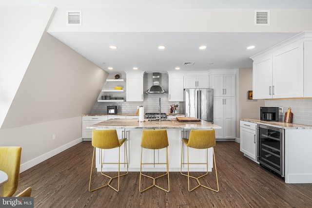 kitchen featuring wine cooler, wall chimney range hood, high end fridge, and white cabinets