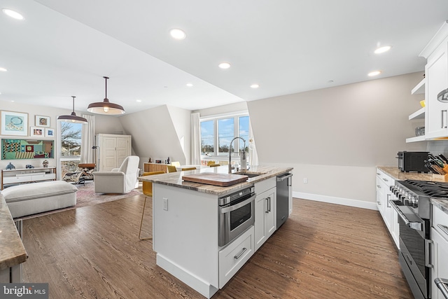 kitchen with appliances with stainless steel finishes, an island with sink, pendant lighting, light stone countertops, and white cabinets