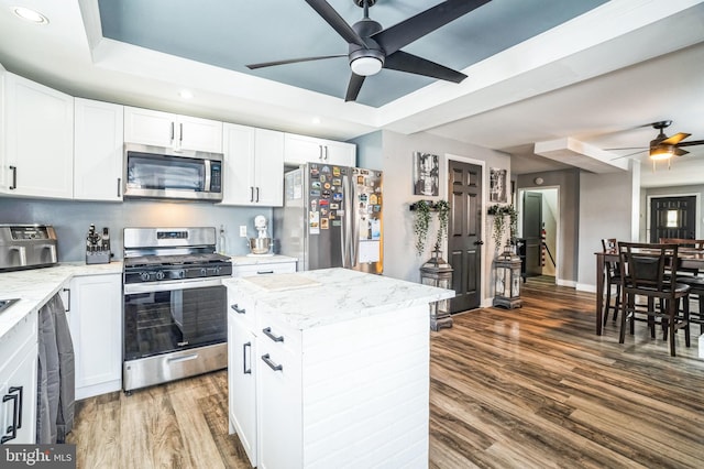 kitchen with a center island, hardwood / wood-style floors, appliances with stainless steel finishes, white cabinetry, and light stone counters