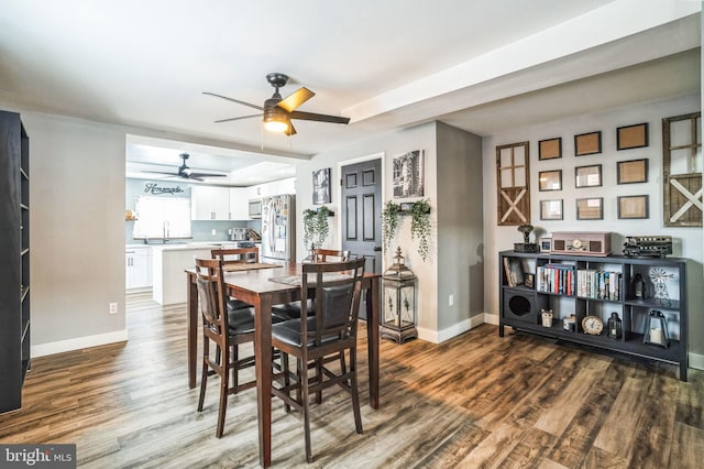 dining space featuring ceiling fan, sink, wood-type flooring, and a tray ceiling