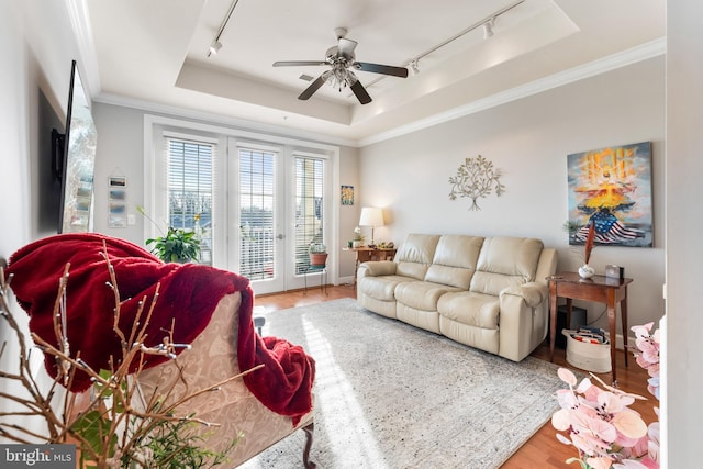 living room featuring rail lighting, crown molding, a raised ceiling, hardwood / wood-style flooring, and ceiling fan