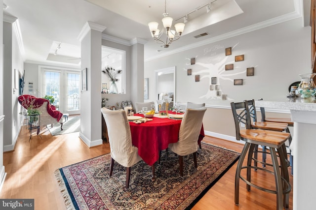 dining space featuring a chandelier, light hardwood / wood-style flooring, track lighting, ornamental molding, and a raised ceiling